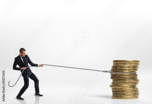 Fototapeta Businessman pulling stack of big golden coins with a rope isolated on white back