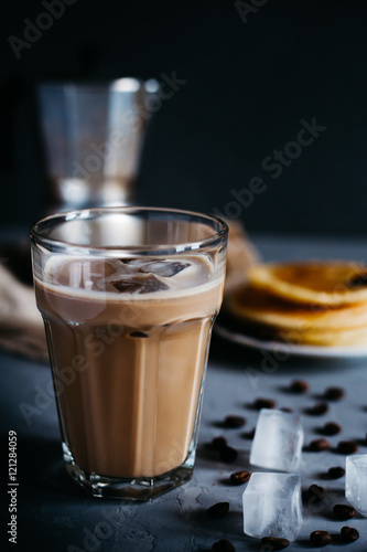 Ice coffee in a high glass, moka coffee maker, a plate of pancakes on a dark gray concrete background, vertical photo