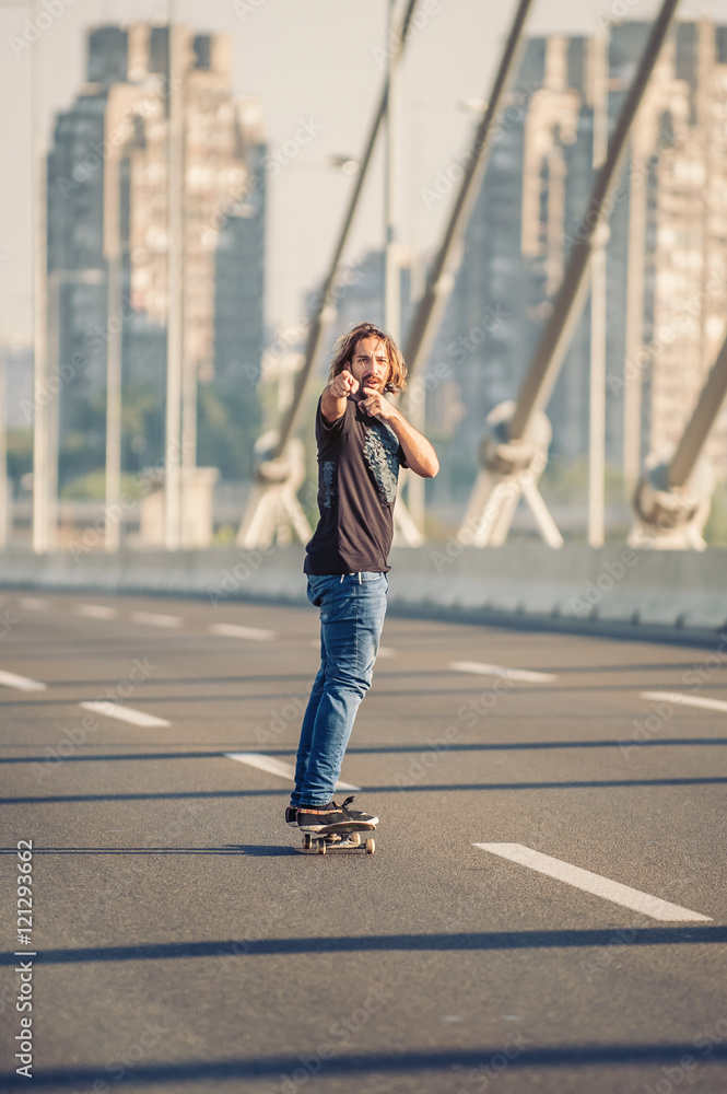 Skateboarder standing on the bridge and pointing to you with his