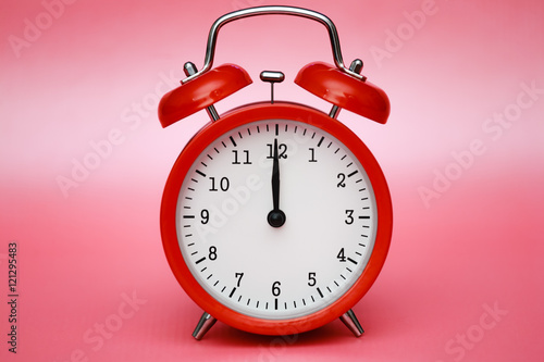 Red vintage alarm clock on pink pastel background.