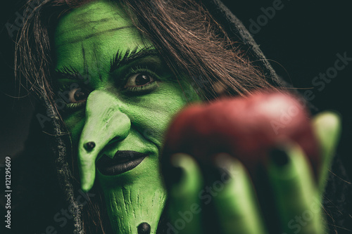 Evil witch looking at camera holding a red apple