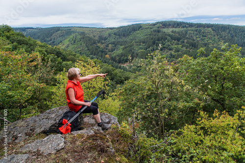 Seniorin sitzt auf einem Felsvorsprung und zeigt mit den Finger; Denntal, Eifel 