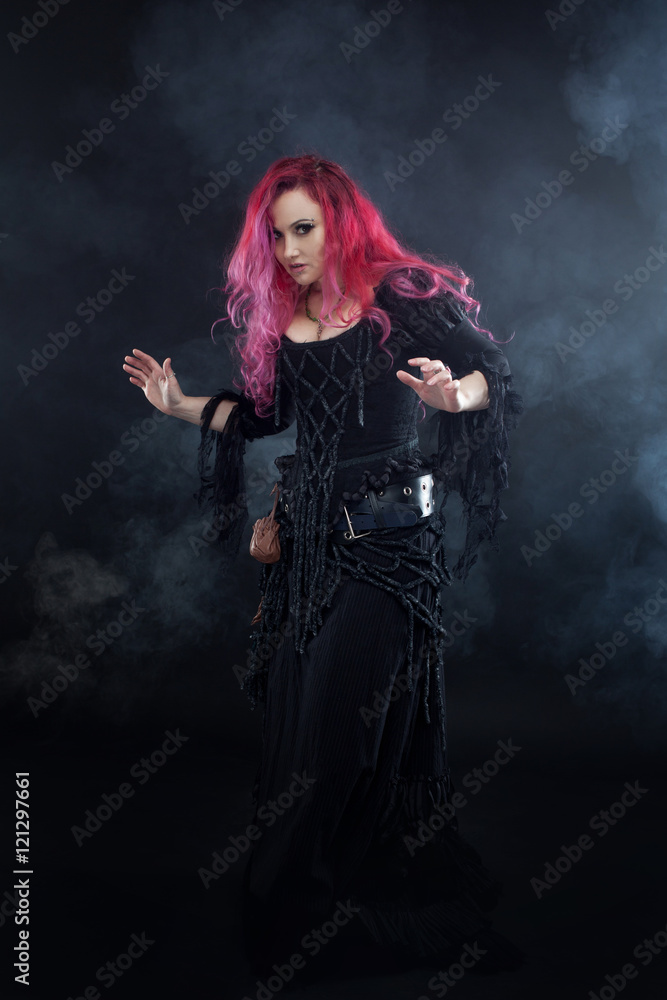 Witch creates magic. Attractive woman with red hair in witches costume