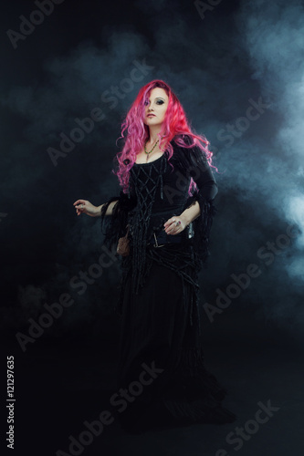 Witch creates magic. Attractive woman with red hair in witches costume