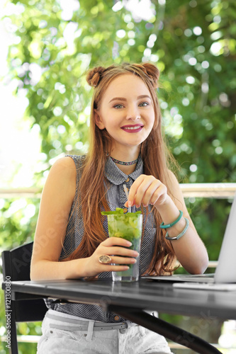 Beautiful teenager girl with laptop and cocktail in cafe