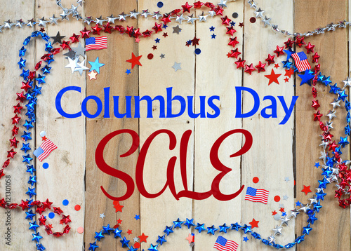 Red, white and blue beads and confetti on rustic wooden background form a border with Columbus Day sale text added photo