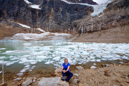 Young woman smiling by alpine lake with icebergs under glacier. Angel Glacier at Mount Edith Cavell. Jasper National Park. Canadian Rockies. Alberta. Canada.