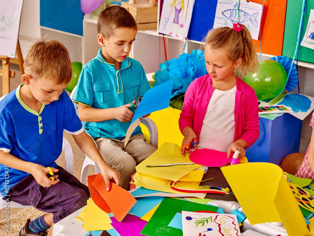 Fototapeta premium Children are making something out of colored paper on table in primary school. Children craft lesson in primary school. Development children craft at class in school. Independent work.