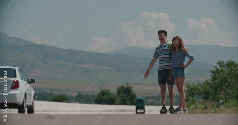young couple standing on an empty road, hitchhiking, mountainous terrain, slow motion young couple standing on an empty road, hitchhiking, mountainous terrain, slow motion
