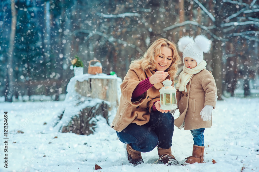 Obraz premium Happy mother and baby daughter walking in snowy winter park. Christmas family time.