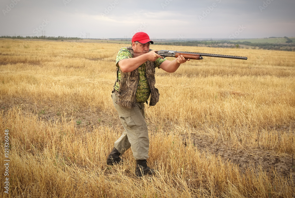 Hunter with a gun on the field aiming at the prey Hunter with a gun on the field aiming at the prey