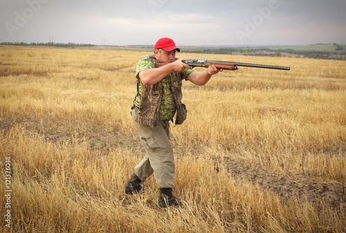 Hunter with a gun on the field aiming at the prey