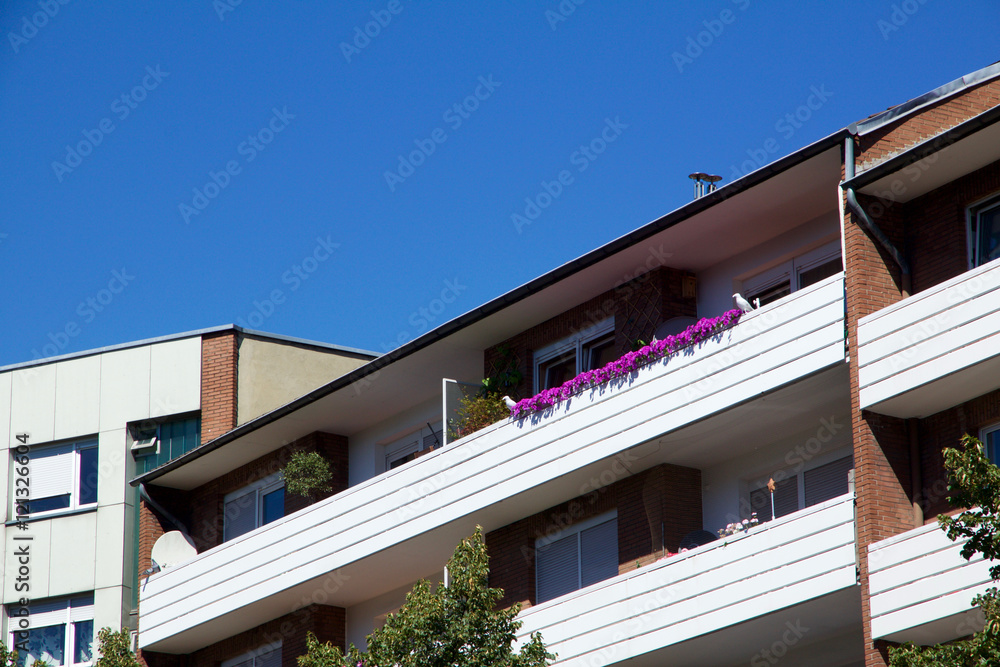 Residential apartment or hotel exterior from street level view. Tree in foreground with blue sky background Residential apartment or hotel exterior from street level view. Tree in foreground with blue sky background