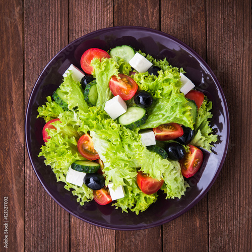 Greek salad (lettuce, tomatoes, feta cheese, cucumbers, black olives) on dark wooden background top view. Healthy food.