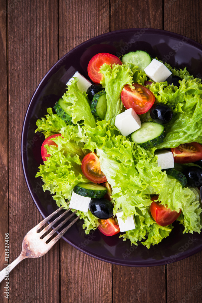 Greek salad (lettuce, tomatoes, feta cheese, cucumbers, black olives) on dark wooden background top view. Healthy food. Greek salad (lettuce, tomatoes, feta cheese, cucumbers, black olives) on dark wooden background top view. Healthy food.