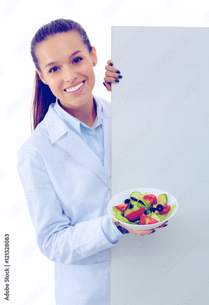 Portrait of a beautiful woman doctor holding a plate with fresh vegetables standing near blank Portrait of a beautiful woman doctor holding a plate with fresh vegetables standing near blank