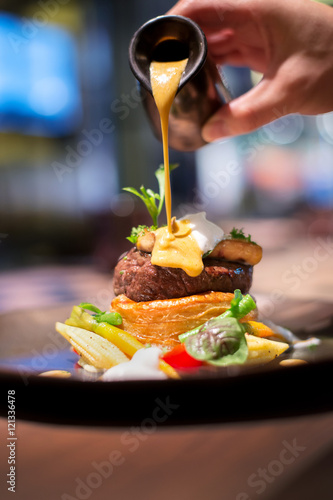 close up chef puring sauce on grilled foie gras topped on tender veal