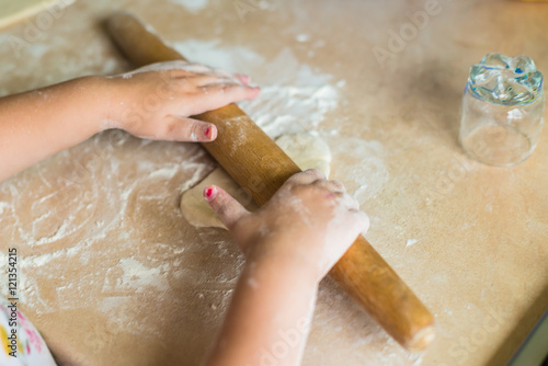 Children's hands holding a rolling pin and roll the dough on the table