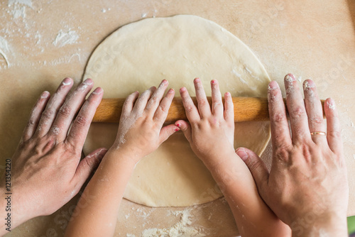 Children and dad hands rolled dough with a rolling pin on the table