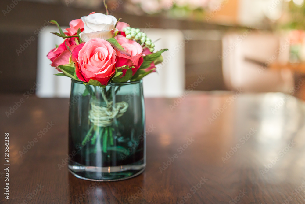 Fototapeta premium Fake roses arranged in a glass on the table.