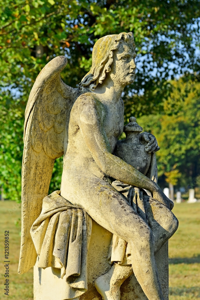 Engelsfigur aus Stein auf einer Wiese am Friedhof Engelsfigur aus Stein auf einer Wiese am Friedhof