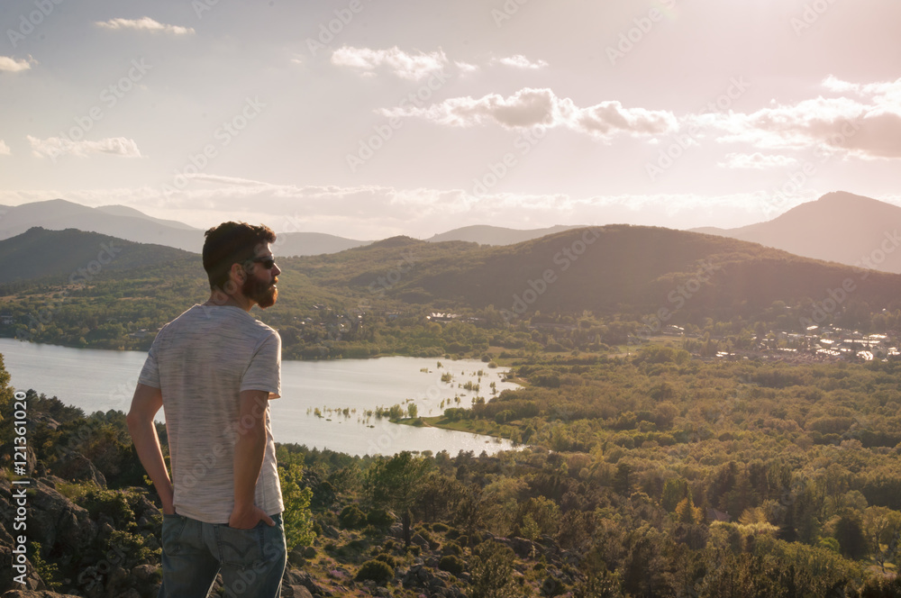 Man watching the sunset on the lake from the top of the hill