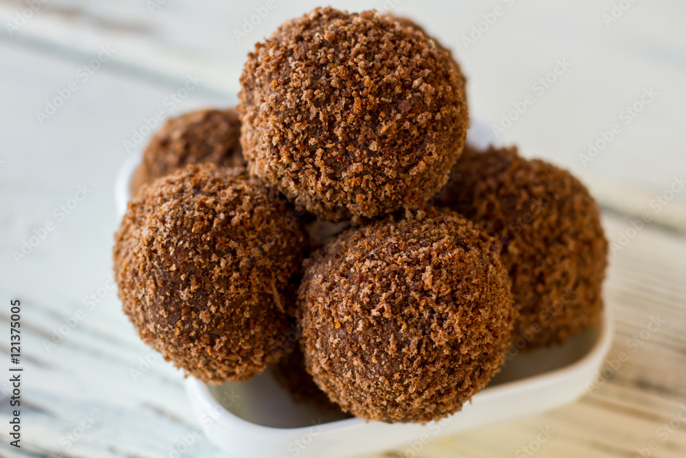 Brown candies covered in crumbs. Sweets in white bowl. Chocolate rum balls. Cocoa powder and cookies. Brown candies covered in crumbs. Sweets in white bowl. Chocolate rum balls. Cocoa powder and cookies.