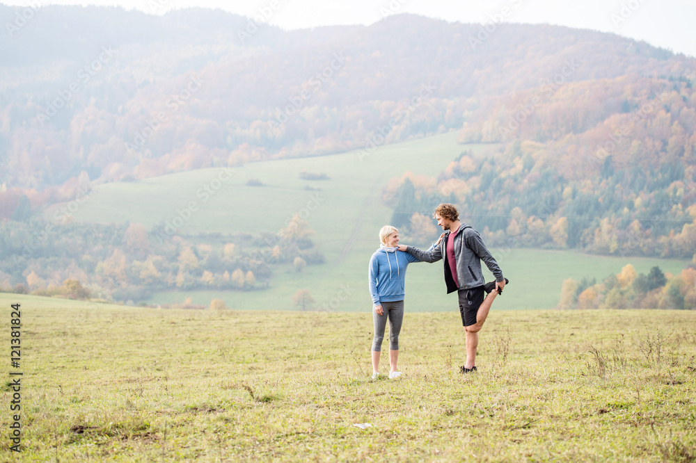 Two young beautiful runners in autumn nature, stretching legs