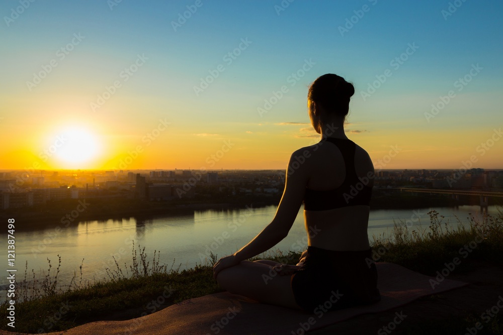 Sporty woman in lotus position in the park at sunset. Sunset light, golden hour, lens flares. Freedom, health and yoga concept.