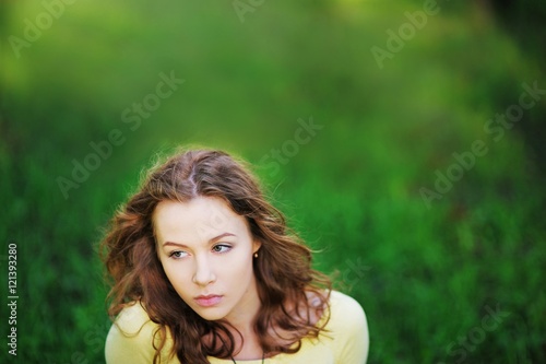 beautiful girl in a yellow jacket sitting on the grass and stares dreamily.