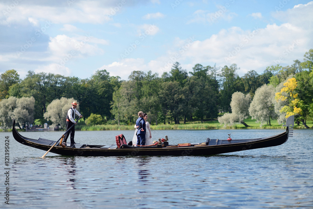 Wedding couple is hugging on a floating gondola. Beauty bride with groom. Beautiful model girl in white dress. Man in suit. Female and male portrait. Woman with lace veil. Cute lady and guy outdoors Wedding couple is hugging on a floating gondola. Beauty bride with groom. Beautiful model girl in white dress. Man in suit. Female and male portrait. Woman with lace veil. Cute lady and guy outdoors