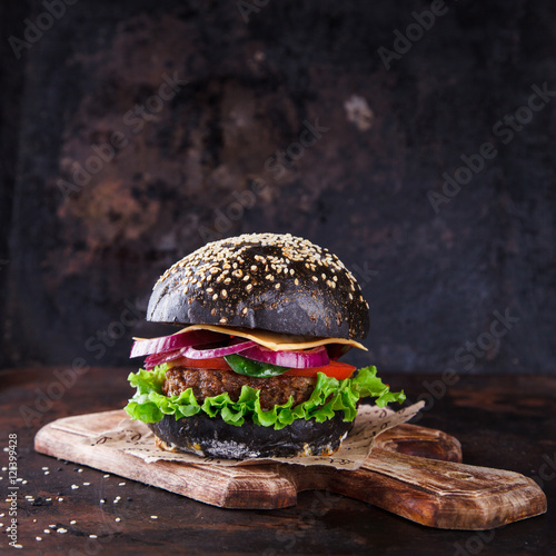Beef burger with a black bun,with lettuce and mayonnaise and ketchup served on pieces of brown paper on a rustic wooden table of counter, on a dark background.selective focus