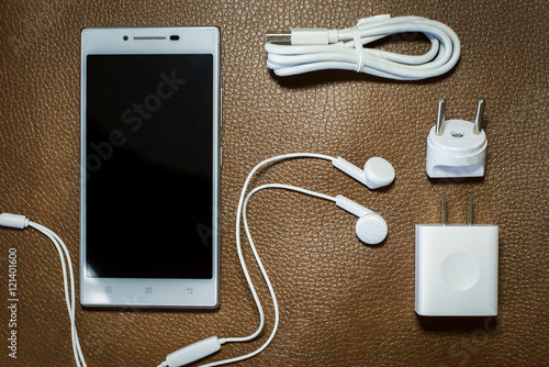 White headphone adapter charger with USB cable and white smartphone on the leather background. 