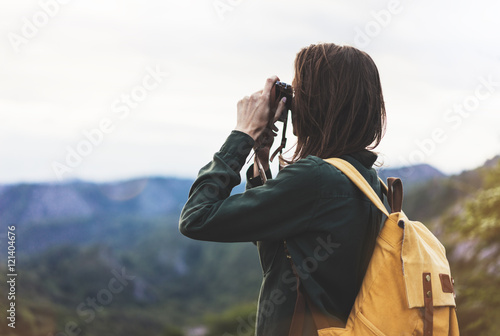 Tourist traveler photographer taking pictures of amazing landscape on vintage photo camera on background valley view mockup sun flare, hipster girl with backpack on peak of foggy mountain
