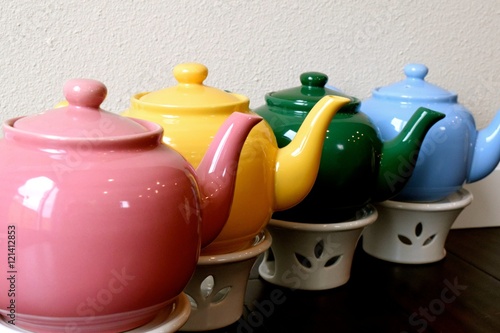Teapots / Pink, yellow, green and blue teapots with warmers, lined up in a row.