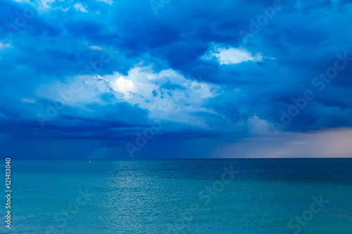 Blue clouds over the ocean at sunset with a storm