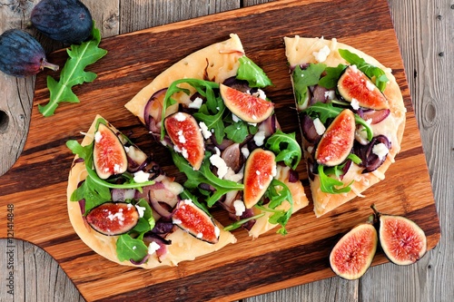 Autumn flat bread pizza with figs, arugula, and goat cheese, overhead view on a paddle board