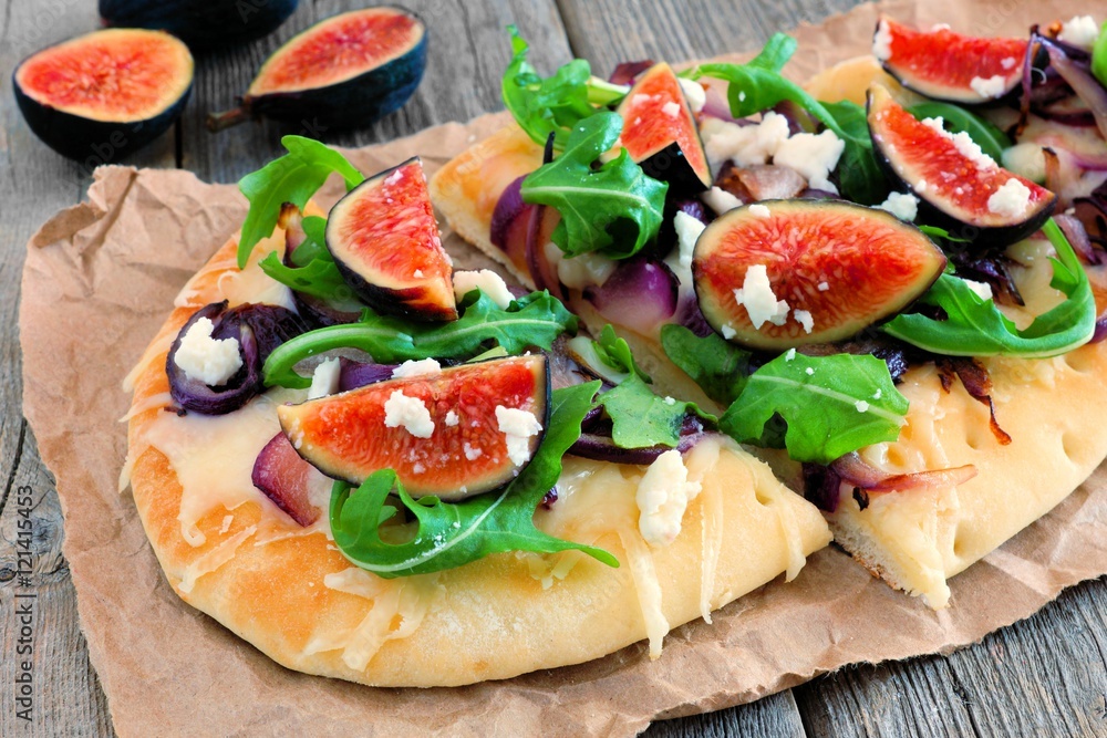 Autumn flat bread pizza with figs, arugula, and goat cheese, close up on wood background