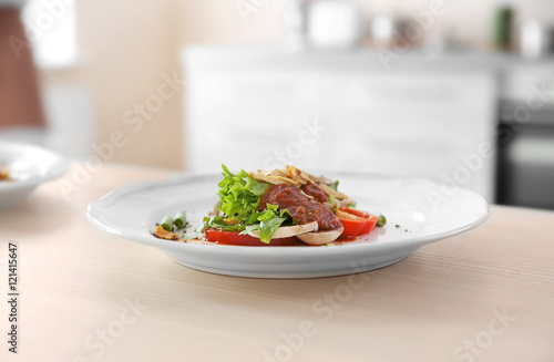 Plate with salad and tomato sauce on table on blurred kitchen background