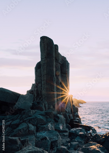 Sun flare as sun rises behind rocks at Bombo Quarry, New South Wales, Australia