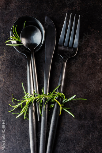 Set of cutlery knife, spoon, fork, rosemary. Black background.