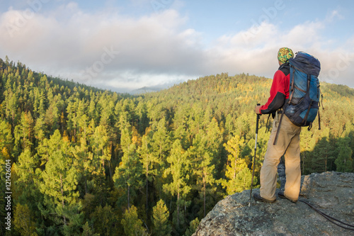 Man with backpack and trekking pole in bandana standing on a roc