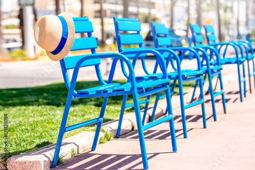 The blue chairs of the promenade with hat in Cannes city. This chairs are iconic symbol and tourist attraction of Cannes in France