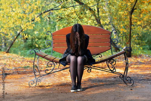 Girl sitting on the bench, covering face with his hands