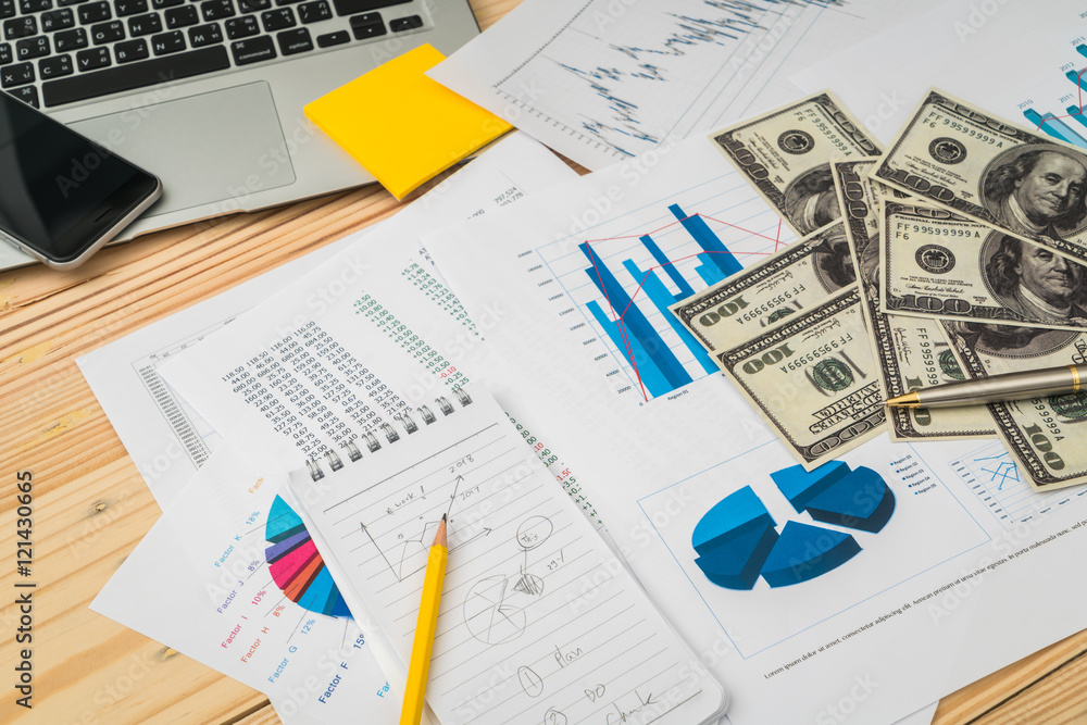 Financial charts on the table with laptop , phone ,dollars bankn Financial charts on the table with laptop , phone ,dollars bankn