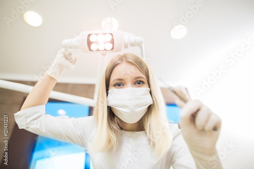 young women dentist with sterile mask readily approaching a patient with dental instruments held in the hands protected with surgical gloves young dentist with sterile mask.Dentist photo