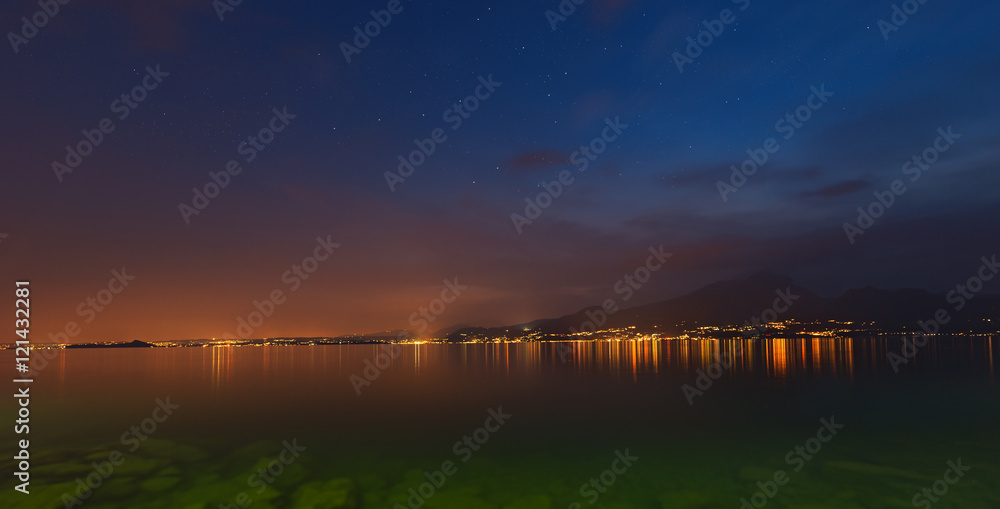 Obraz premium Lago di Garda at night (Garda Lake), with the lights of the coast and starry sky, Italy
