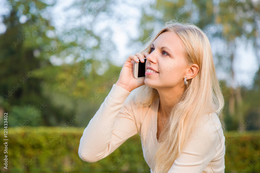 Young, beautiful woman speaking on the phone in the park in summer evening. Young, beautiful woman speaking on the phone in the park in summer evening.