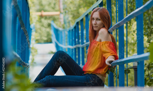 Young woman with red hair and yellow jacket sitting on a small bridge in summer day photo