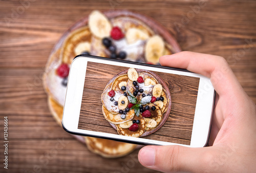 Hands taking photo pancakes with fresh fruit  with smartphone.